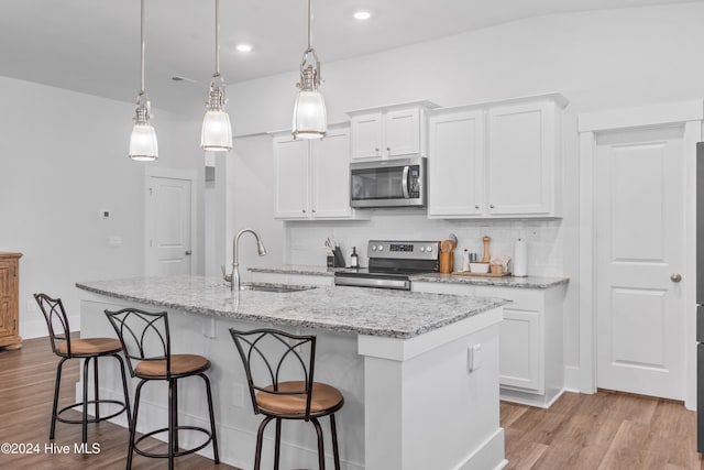 kitchen featuring a center island with sink, sink, appliances with stainless steel finishes, decorative light fixtures, and white cabinetry