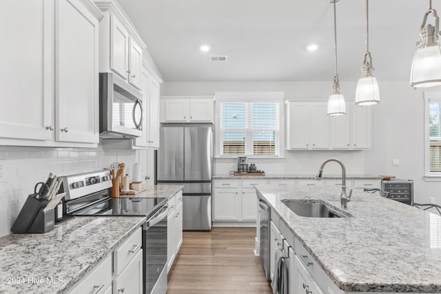 kitchen with white cabinetry, sink, stainless steel appliances, decorative light fixtures, and a center island with sink