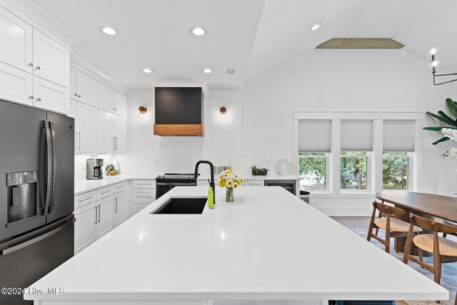 kitchen with backsplash, sink, vaulted ceiling, stainless steel fridge, and an island with sink