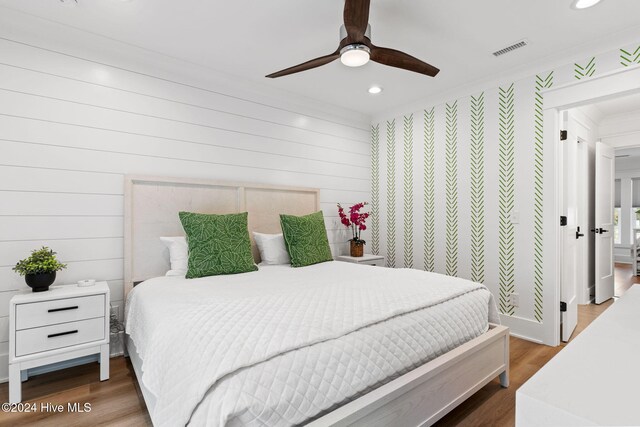 bedroom with ceiling fan, wood walls, and hardwood / wood-style flooring