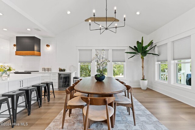 dining room with wine cooler, light hardwood / wood-style flooring, high vaulted ceiling, and an inviting chandelier