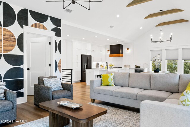 living room featuring beamed ceiling, light wood-type flooring, high vaulted ceiling, and a chandelier