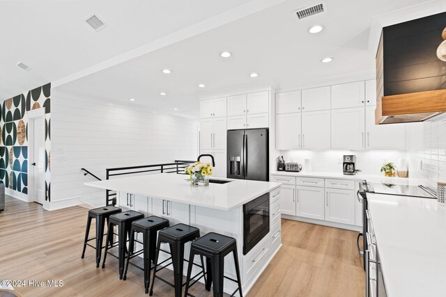 kitchen featuring a kitchen breakfast bar, stainless steel appliances, a center island with sink, light hardwood / wood-style floors, and white cabinetry