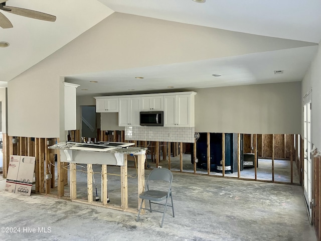 kitchen with backsplash, white cabinetry, concrete flooring, and vaulted ceiling