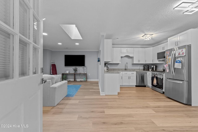 kitchen featuring appliances with stainless steel finishes, a skylight, a textured ceiling, crown molding, and white cabinets