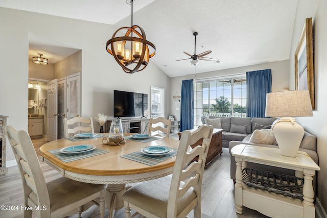 dining room featuring ceiling fan with notable chandelier, light hardwood / wood-style flooring, and vaulted ceiling