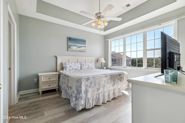 bedroom with hardwood / wood-style floors, a raised ceiling, and ceiling fan