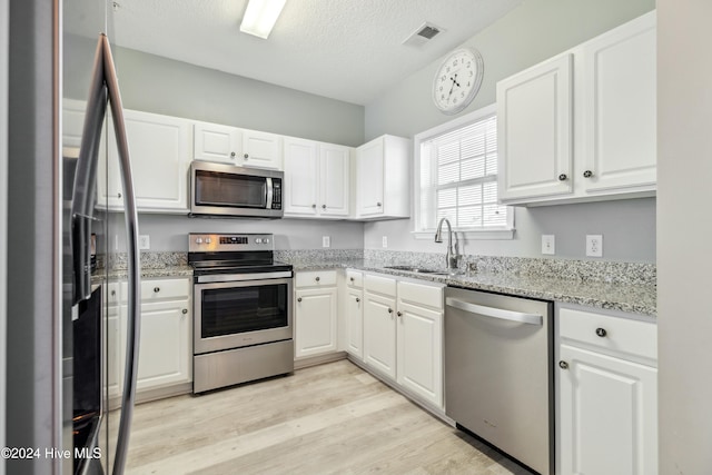 kitchen with light stone countertops, white cabinetry, sink, stainless steel appliances, and light wood-type flooring