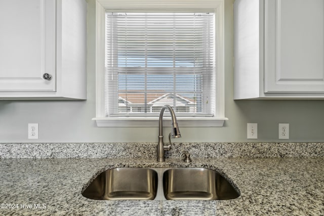 room details featuring white cabinets, light stone counters, and sink