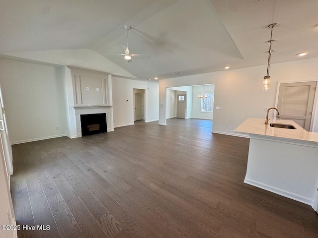 unfurnished living room with lofted ceiling, ceiling fan with notable chandelier, a fireplace, a sink, and dark wood-style floors