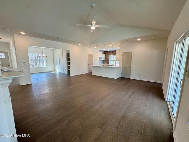 unfurnished living room with ceiling fan with notable chandelier, vaulted ceiling, dark wood finished floors, and recessed lighting