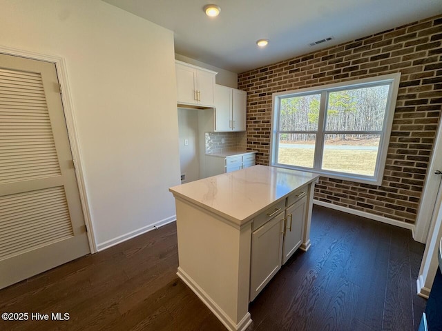 kitchen featuring brick wall, dark wood-style flooring, visible vents, and white cabinets