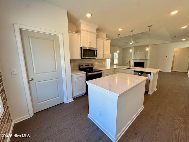 kitchen featuring appliances with stainless steel finishes, dark wood-type flooring, a center island, a peninsula, and a sink