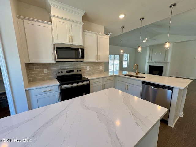 kitchen with a peninsula, a sink, open floor plan, appliances with stainless steel finishes, and backsplash