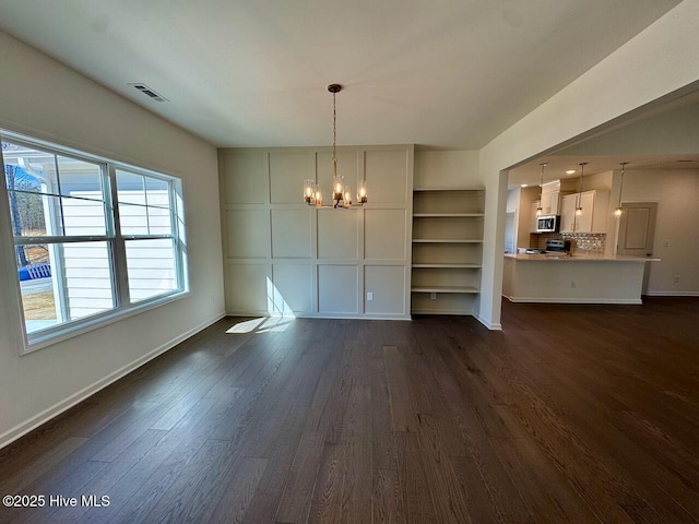 unfurnished dining area featuring dark wood finished floors, visible vents, a notable chandelier, and baseboards