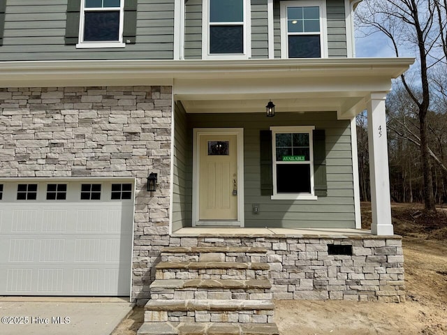 entrance to property with a garage, stone siding, and covered porch