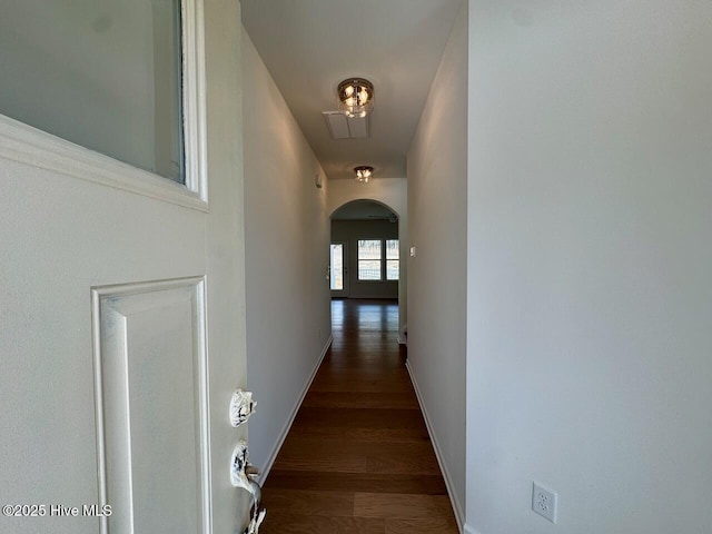 corridor featuring arched walkways, baseboards, and wood finished floors