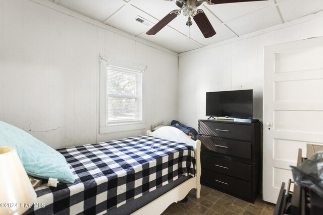 bedroom featuring ceiling fan, a drop ceiling, and wooden walls