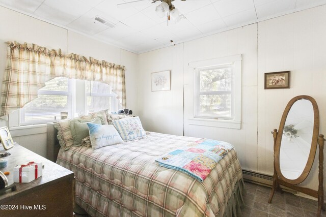 bedroom with ceiling fan, baseboard heating, and multiple windows