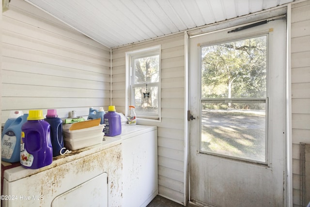 doorway to outside with washing machine and clothes dryer, wood walls, a healthy amount of sunlight, and vaulted ceiling