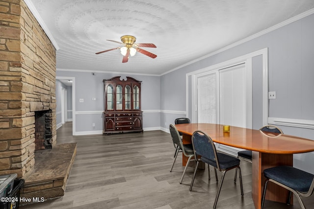 dining room featuring dark hardwood / wood-style flooring, a stone fireplace, ceiling fan, and crown molding