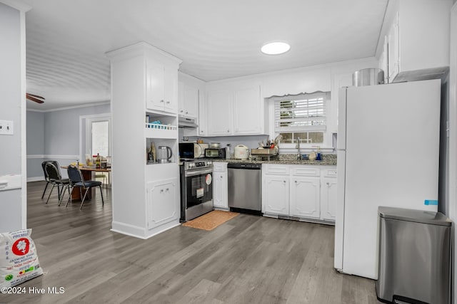 kitchen featuring ornamental molding, dark stone counters, stainless steel appliances, light hardwood / wood-style flooring, and white cabinets