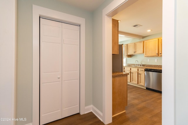 kitchen with dark wood-type flooring, light brown cabinets, stainless steel dishwasher, and sink