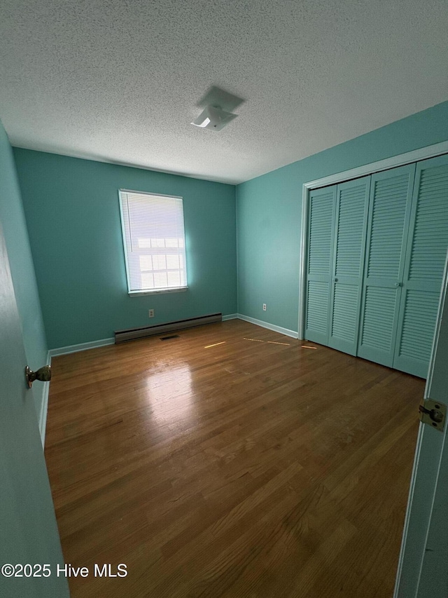 unfurnished bedroom featuring a baseboard radiator, dark hardwood / wood-style floors, a closet, and a textured ceiling