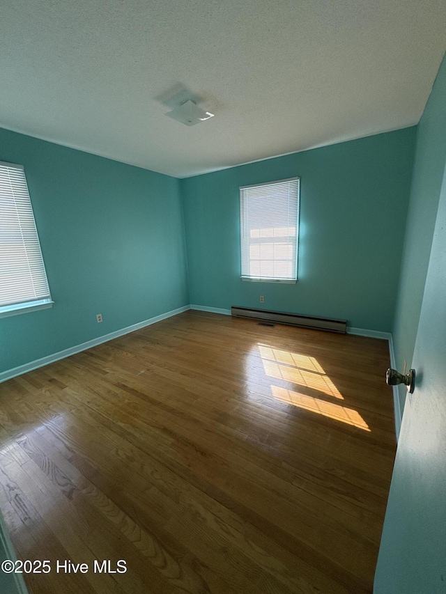 spare room featuring light hardwood / wood-style floors, a textured ceiling, and a baseboard heating unit