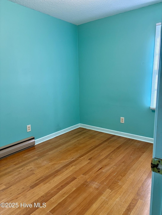 unfurnished room featuring a baseboard heating unit, a textured ceiling, and light wood-type flooring