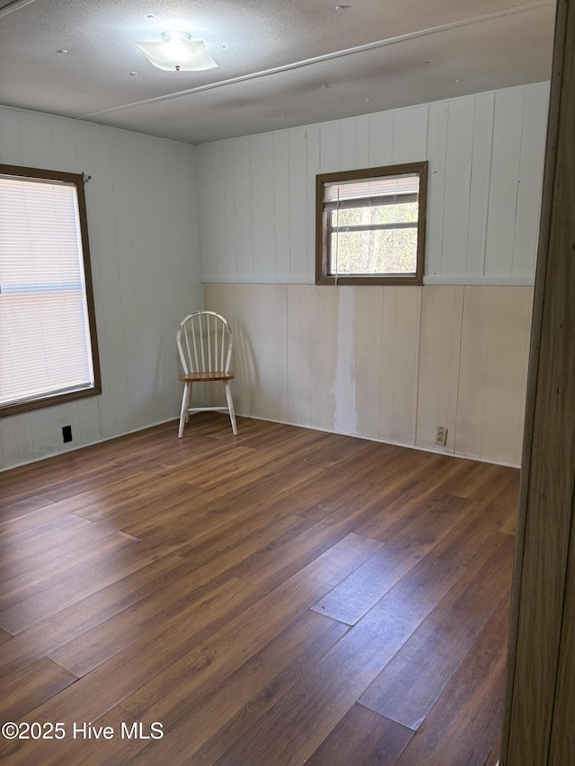 unfurnished room featuring wooden walls, a textured ceiling, and dark hardwood / wood-style flooring