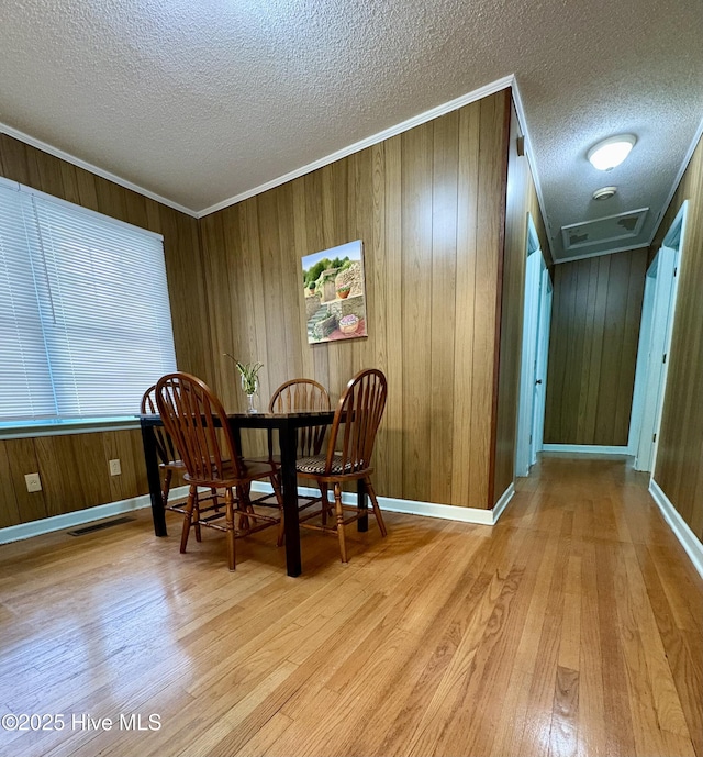 dining area with ornamental molding, light hardwood / wood-style floors, a textured ceiling, and wood walls