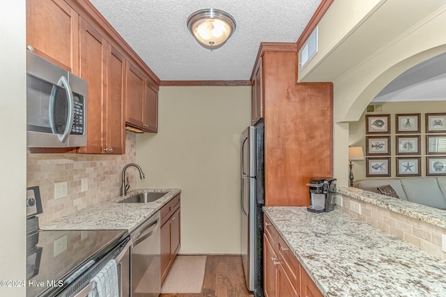 kitchen featuring sink, stainless steel appliances, light stone counters, decorative backsplash, and light wood-type flooring