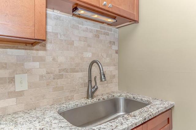 kitchen with backsplash, light stone countertops, and sink