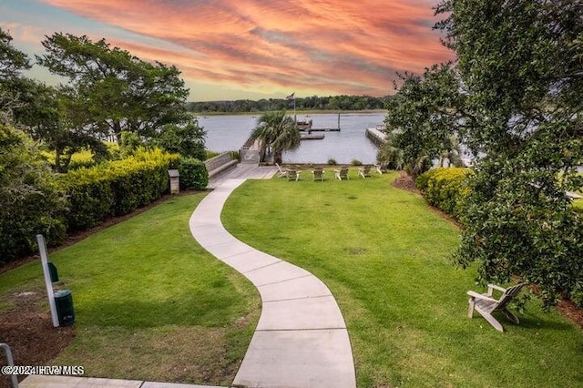 view of property's community with a dock, a lawn, and a water view