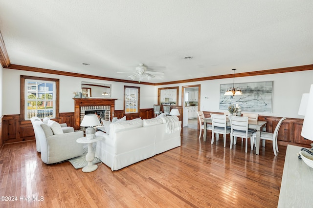 living room featuring a brick fireplace, ceiling fan with notable chandelier, a textured ceiling, crown molding, and light hardwood / wood-style flooring