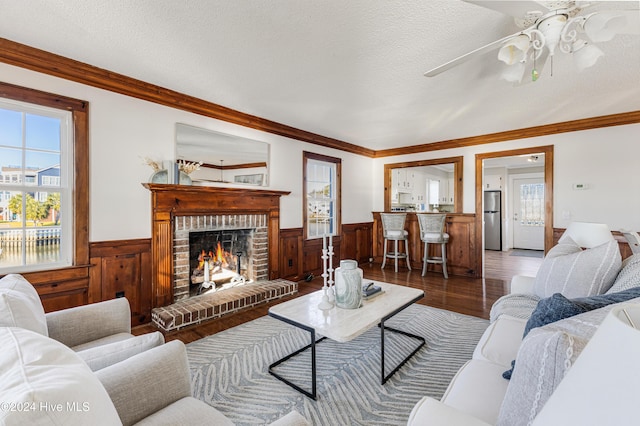 living room with ceiling fan, hardwood / wood-style floors, a textured ceiling, a fireplace, and ornamental molding