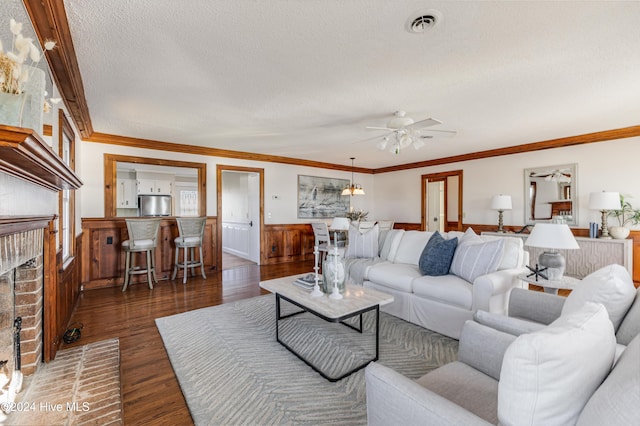 living area with crown molding, visible vents, dark wood-type flooring, a brick fireplace, and a textured ceiling