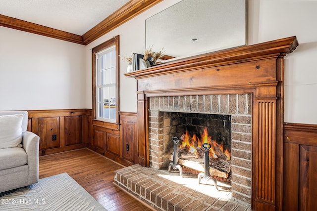 living room with crown molding, wood finished floors, a textured ceiling, a wainscoted wall, and a brick fireplace