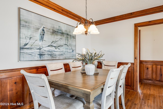 dining space with a textured ceiling, a chandelier, ornamental molding, wainscoting, and wood-type flooring