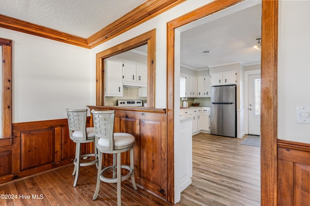 bar featuring wood finished floors, a textured ceiling, a wainscoted wall, ornamental molding, and freestanding refrigerator