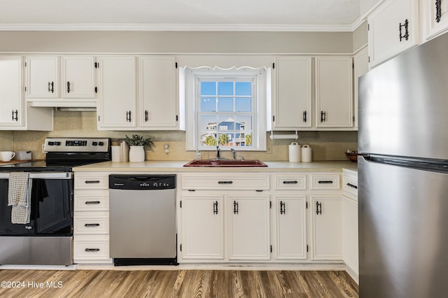 kitchen with white cabinets, ornamental molding, wood finished floors, stainless steel appliances, and a sink