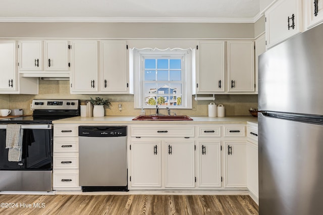 kitchen with white cabinets, wood finished floors, ornamental molding, a sink, and appliances with stainless steel finishes