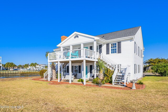 rear view of house with a lawn, a deck with water view, stairway, and a chimney