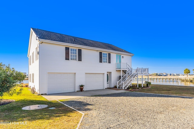 view of front facade with an attached garage, a water view, stairway, a front yard, and gravel driveway