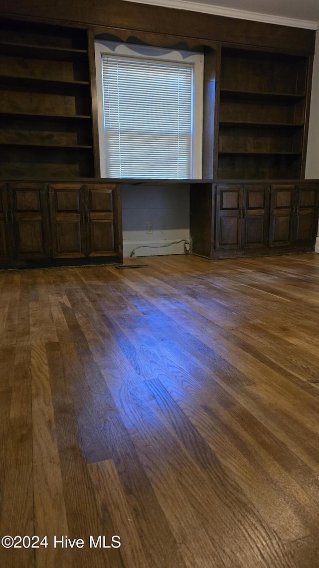 unfurnished living room with built in shelves, dark hardwood / wood-style flooring, and crown molding