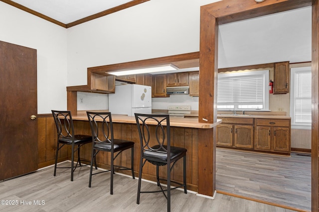 kitchen with white appliances, ornamental molding, light hardwood / wood-style floors, kitchen peninsula, and a breakfast bar area