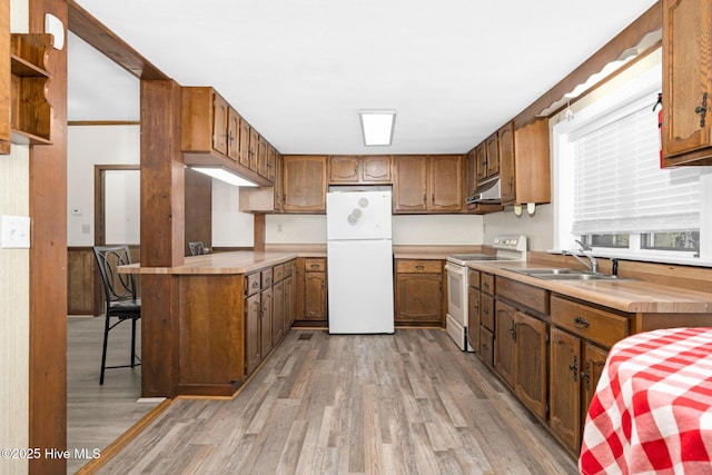 kitchen with white appliances, light wood-type flooring, wooden walls, and sink