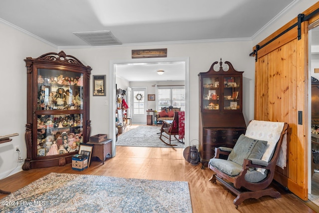 sitting room with a barn door, light hardwood / wood-style flooring, and ornamental molding