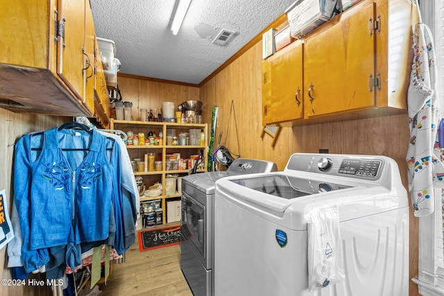 laundry room featuring cabinets, wooden walls, light hardwood / wood-style flooring, separate washer and dryer, and a textured ceiling